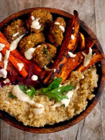 Falafel with a tahini sauce, sweet potato fries, roast carrots and Quinoa in wooden bowl on table