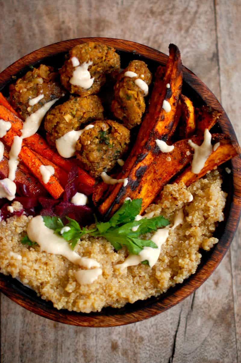 Falafel with a tahini sauce, sweet potato fries, roast carrots and Quinoa in wooden bowl on table