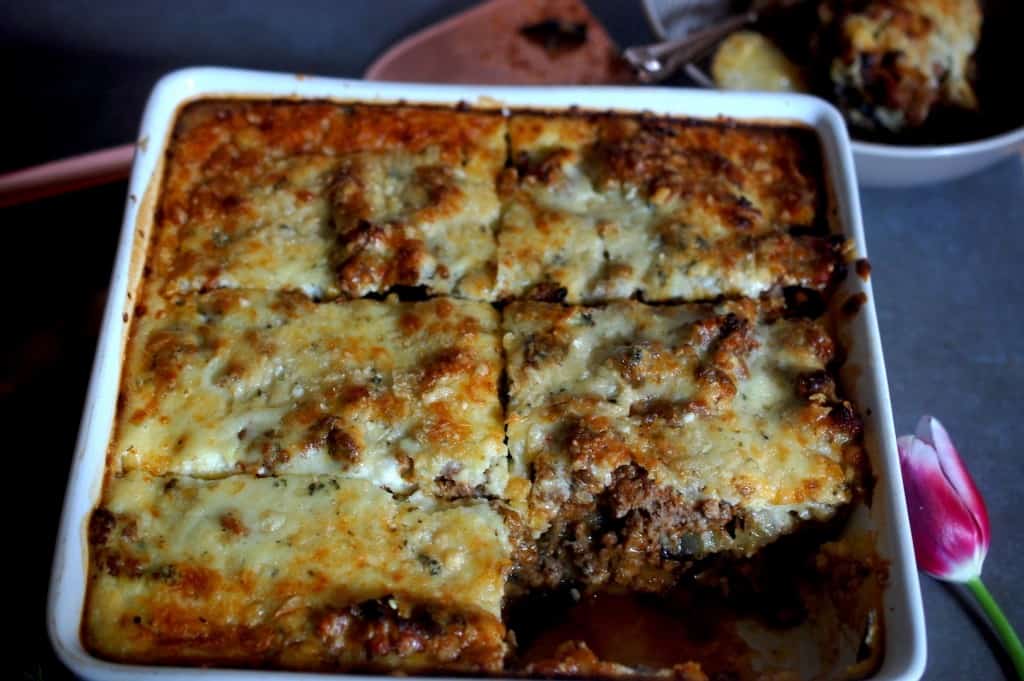 Moussaka in a square baking dish, one slice in bowl