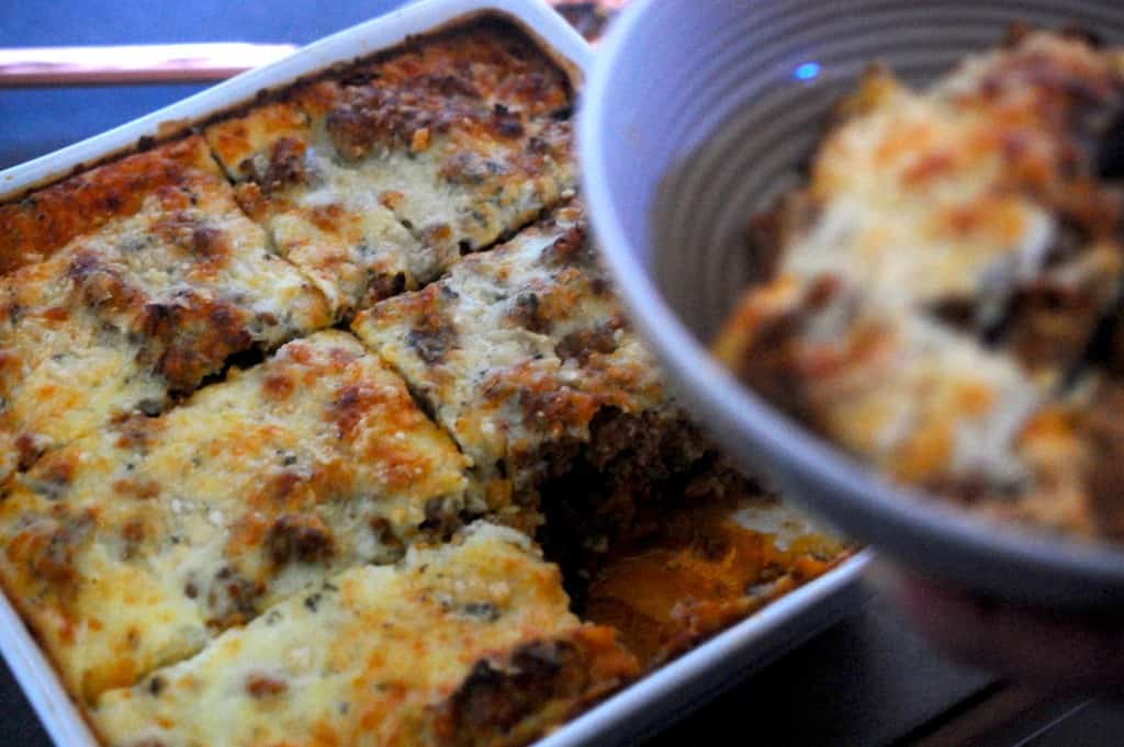 Moussaka cut into slices in baking dish with one slice in bowl