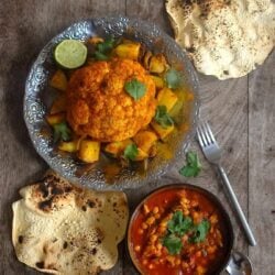 Chicken and chickpea curry on table with popadoms and whole roast cauliflower