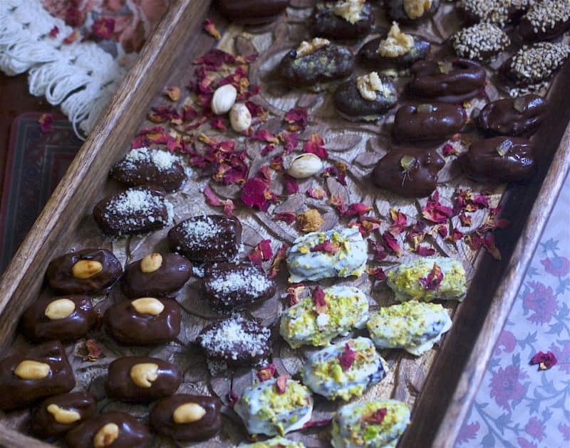 Various chocolate dates on a wooden tray with rose petals