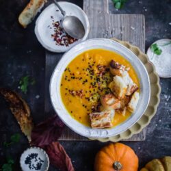 Butternut Squash Soup on a board with crusty bread and pumpkins to side