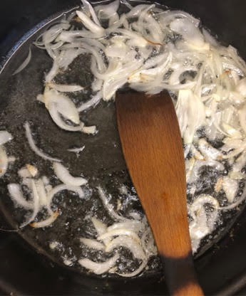 Onions being fried in oil with wooden spatula
