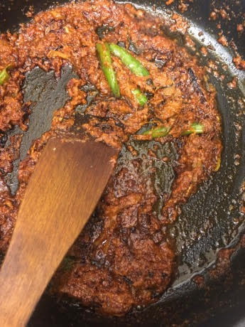Masala with most of water burnt off in pan with wooden spatula