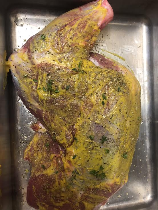 Lamb shoulder with mustard, herbs and salt and pepper in roasting tin