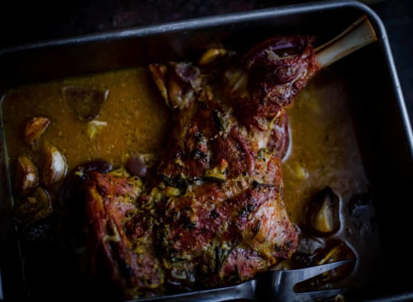 Lamb shoulder in a pan with juices, onions and garlic around it