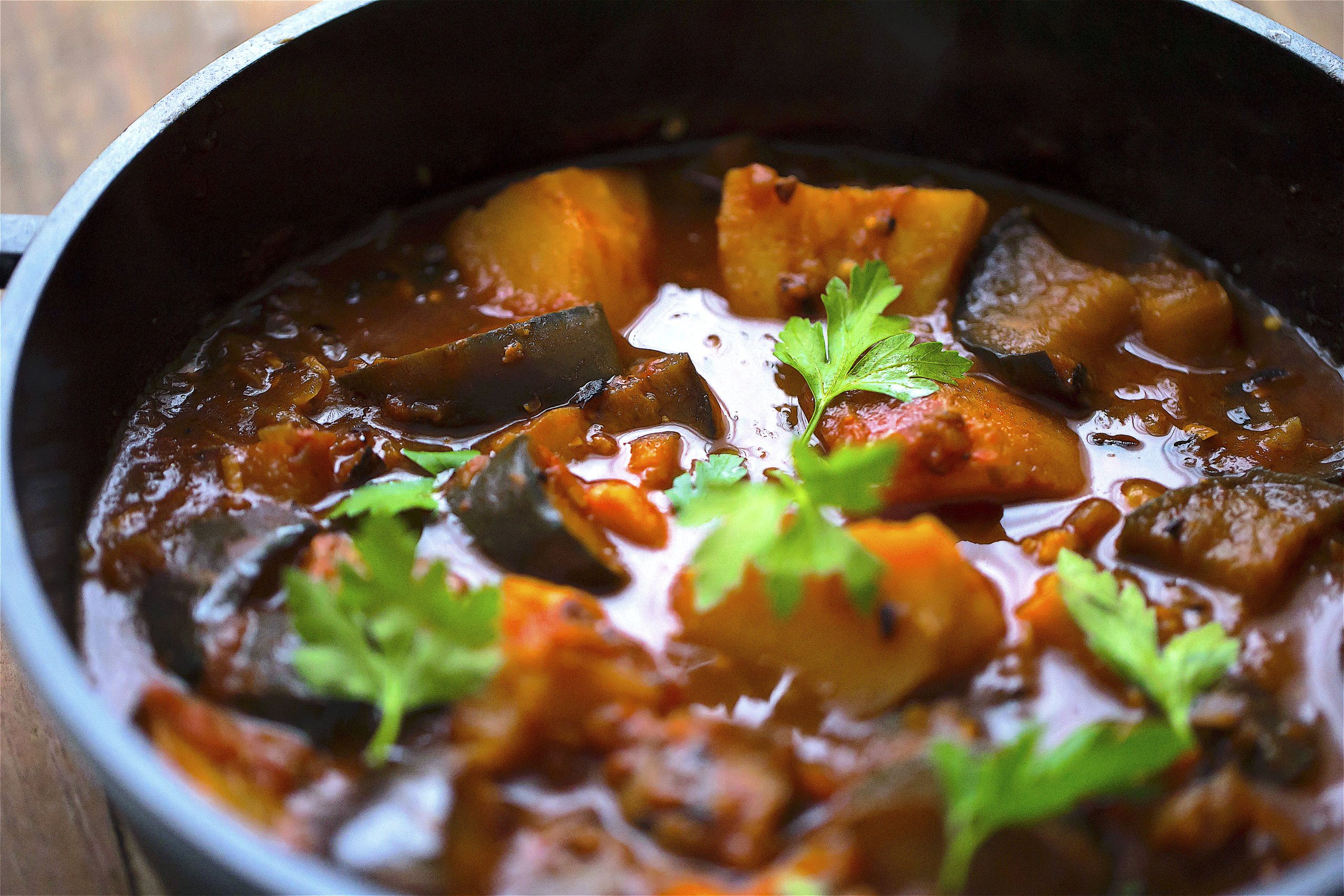 Aubergine curry with potato and coriander in a pot on table