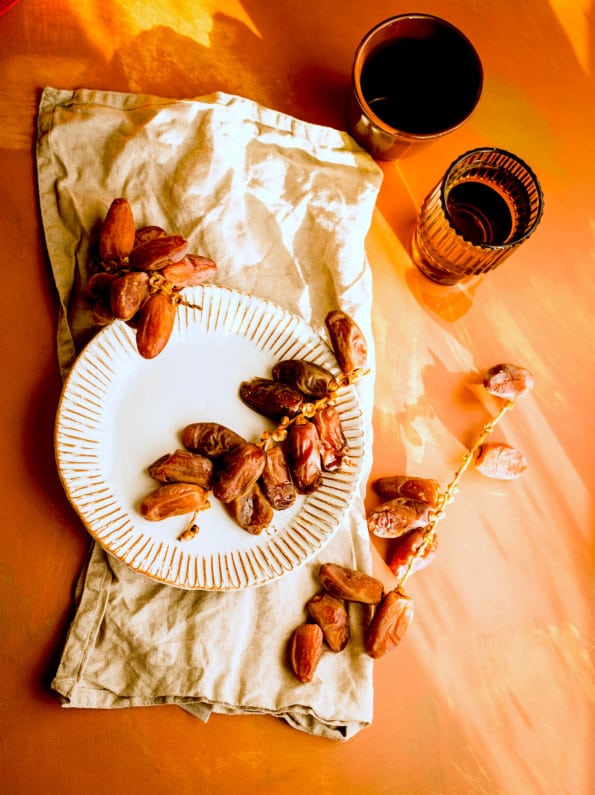 Dates in a white plate with 2 cups of water to the side