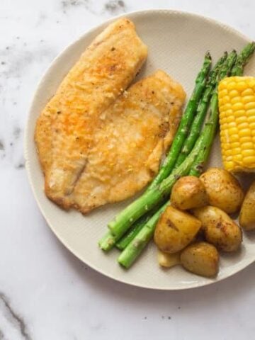 Fish with asparagus, corn on the cob and potatoes on a plate on marble background