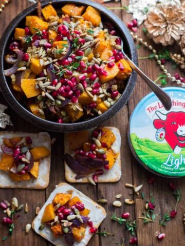 Butternut squash salad in bowl topped with seeds. 3 crackers with laughing cow spread and topped with squash salad on wooden table.