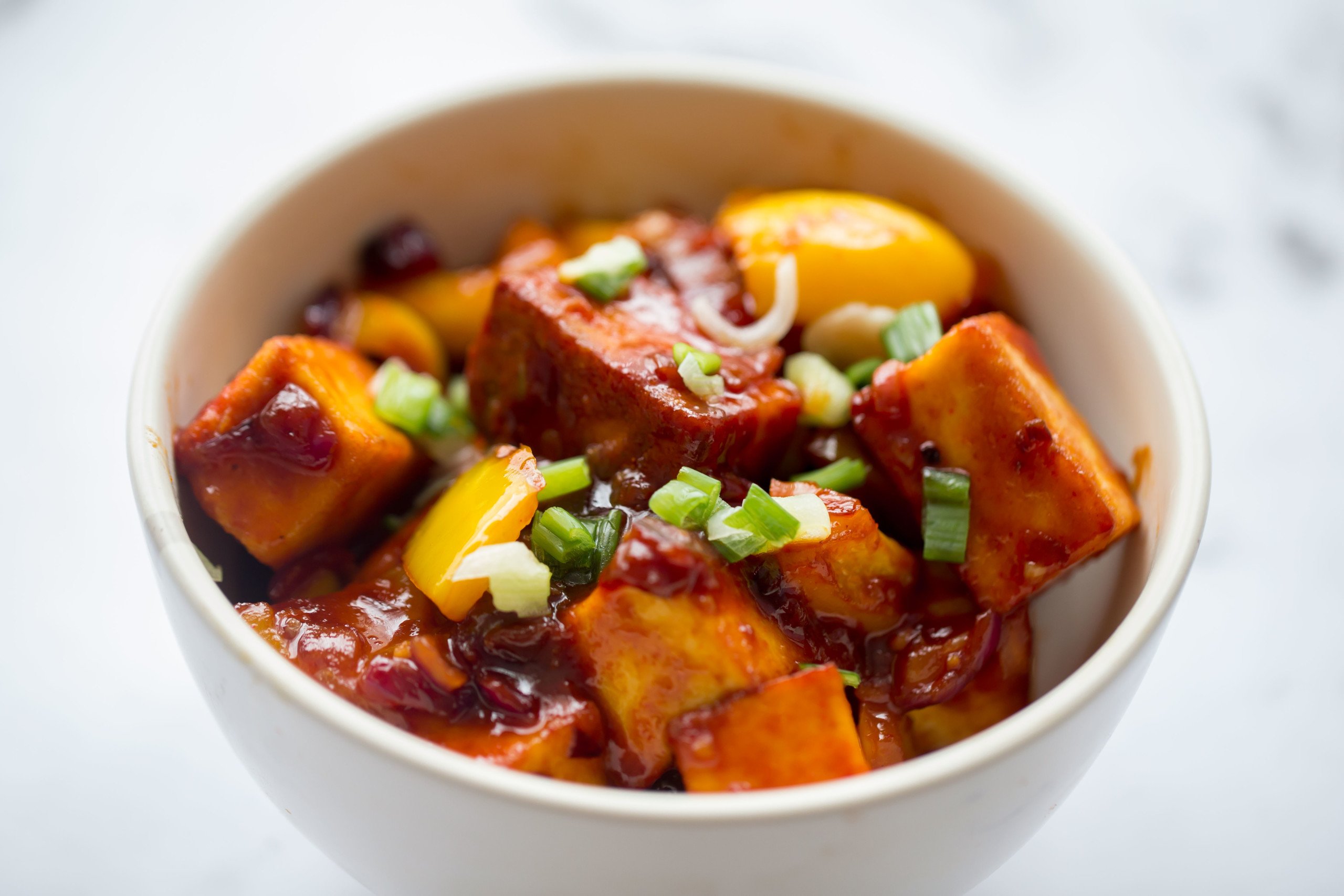 Chilli Paneer with Peppers in a white bowl, topped with spring onions