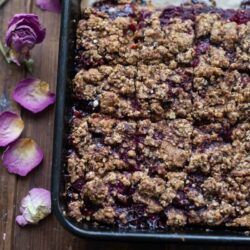 Cherry and Raspberry Crumble Breakfast Bars in baking tray with flowers next to tray