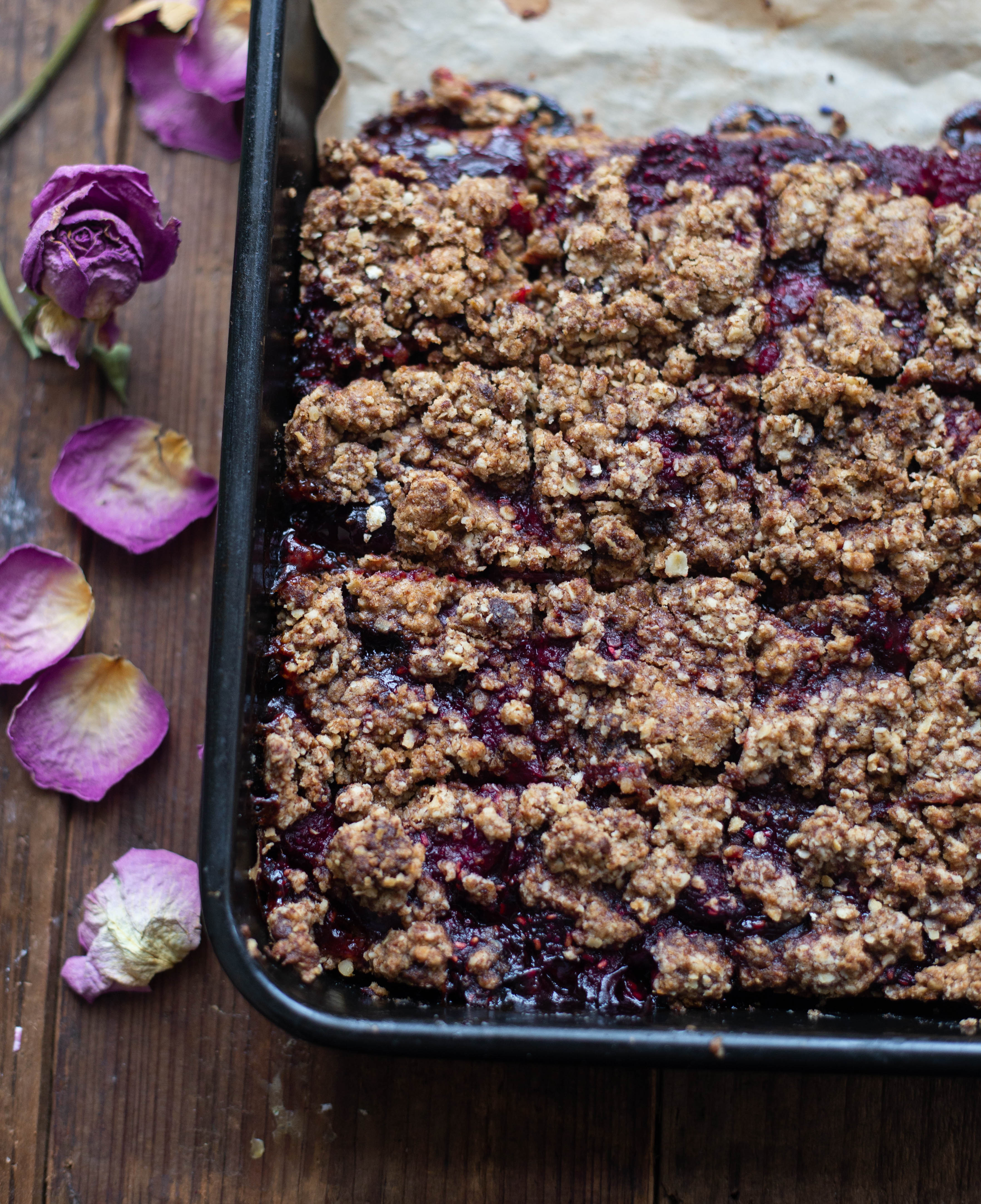 Cherry and Raspberry Crumble Breakfast Bars in baking tray with flowers next to tray