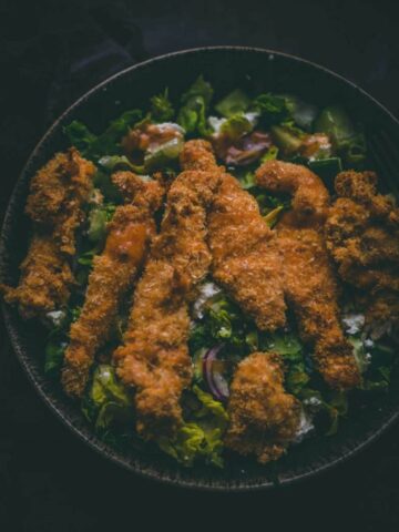 Crispy Almond Flour Chicken Strips on a bed of salad in a large bowl