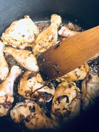 Browned Onions and spices in a pot with browned chicken and wooden spatula