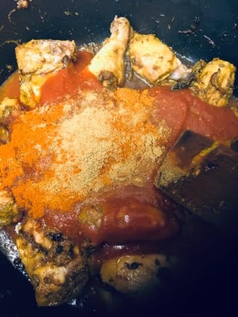 Chicken and spices and tomato in large pot with wooden spatula, pre mixed