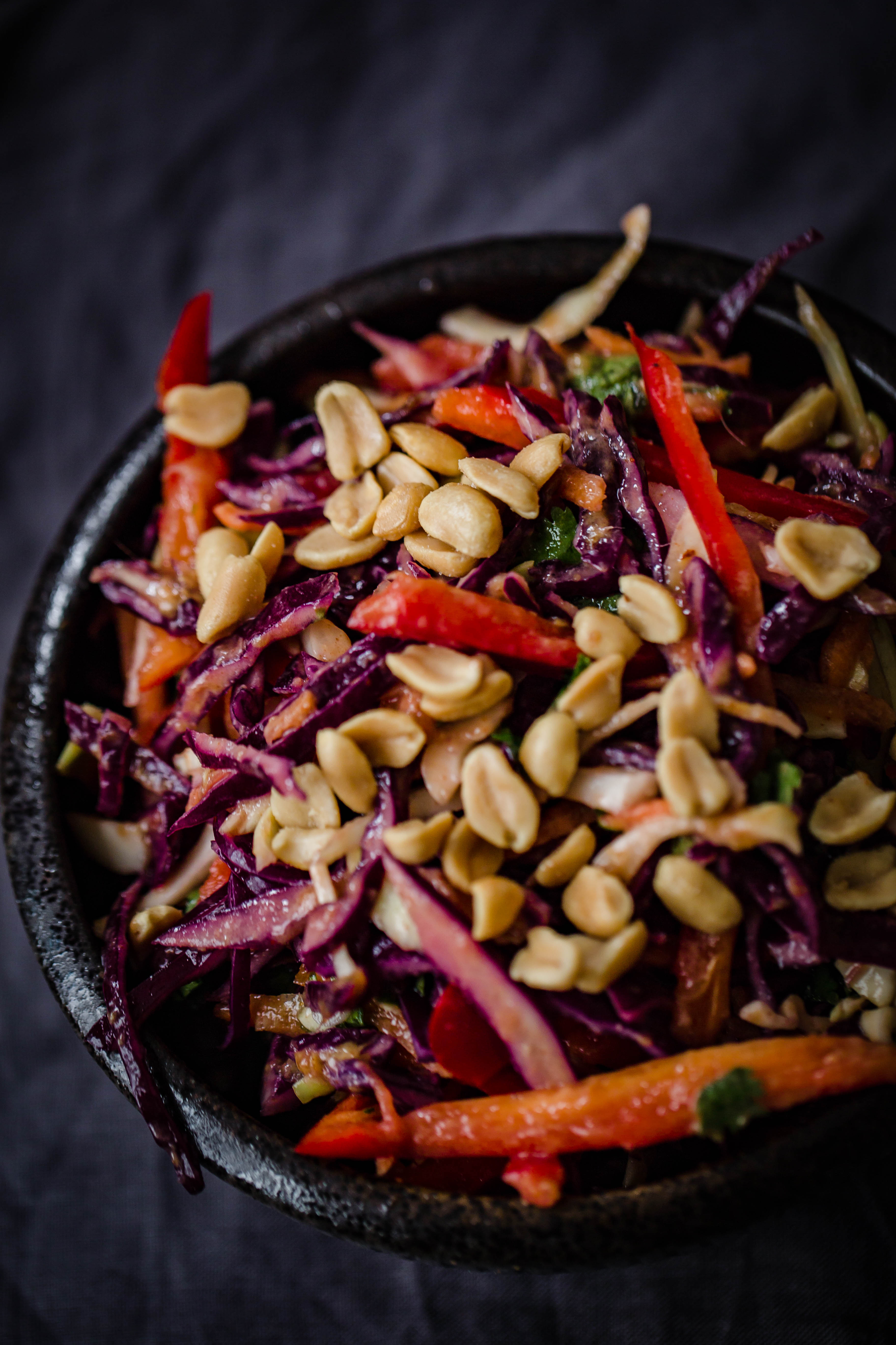 Red Cabbage, Red Pepper, Coriander and Peanuts in a black bowl on a grey creased towel