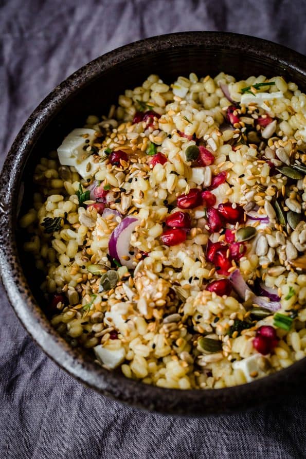 Barley Salad with feta, pomegranate, red onion and mixed seeds and fennel in black bowl on grey towel