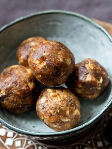 Date and Peanut Butter Balls in a small blue bowl on a patterned wooded circular board