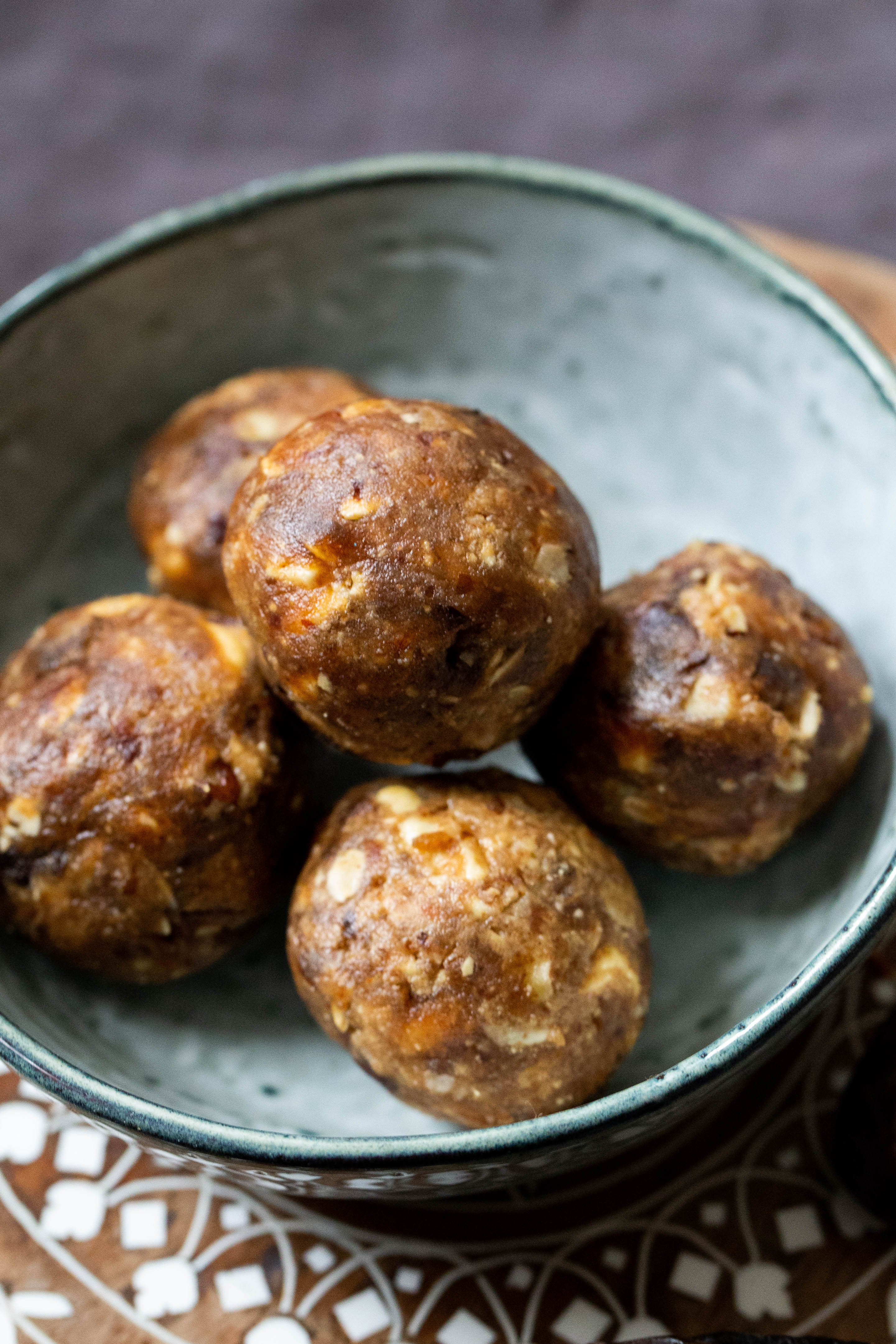 Date and Peanut Butter Balls in a small blue bowl on a patterned wooded circular board
