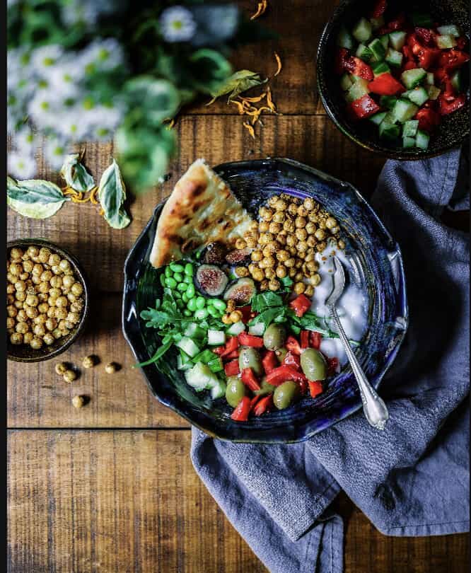 Chickpea and salad bowl with pitta and spoon on towel, chickpeas to side and salad to rear, daisies on table