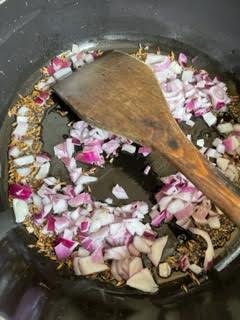 Onions added to pot with wooden spoon