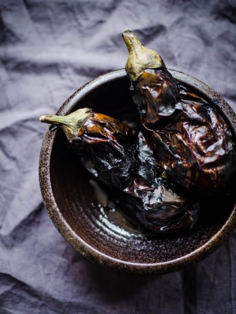 2 charred Aubergines in a black bowl on a grey background