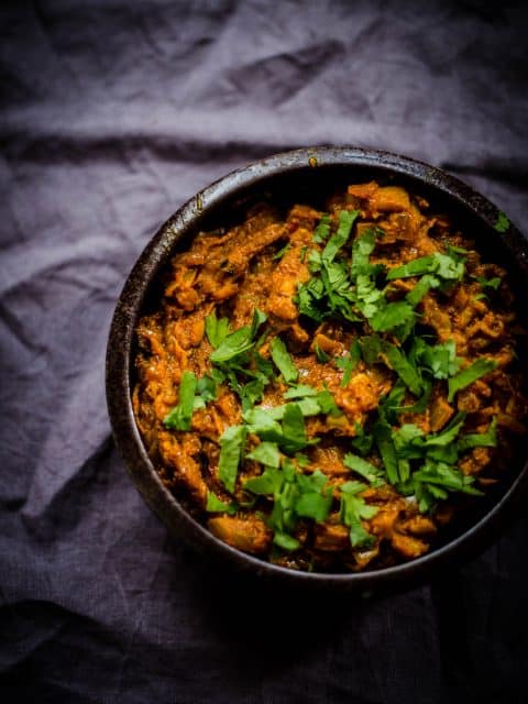 Baingan Barta in a black dish with coriander scattered over on a grey background