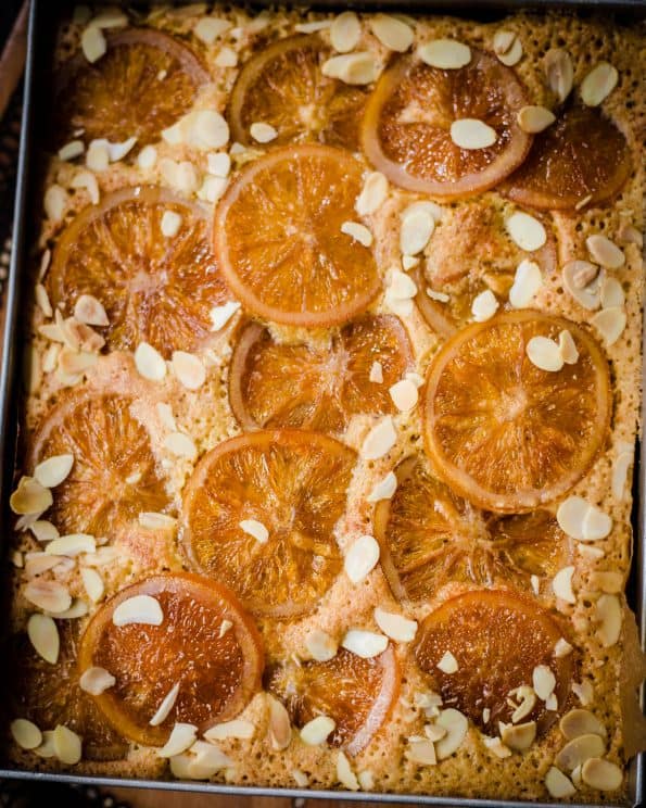 Sticky Orange Cake in tray with sliced oranges and flaked almonds on top