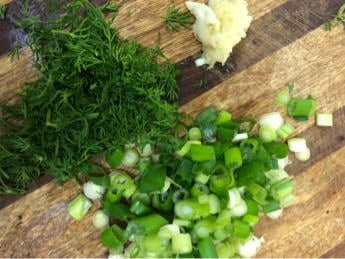 Chopped spring onions, garlic and dill on board