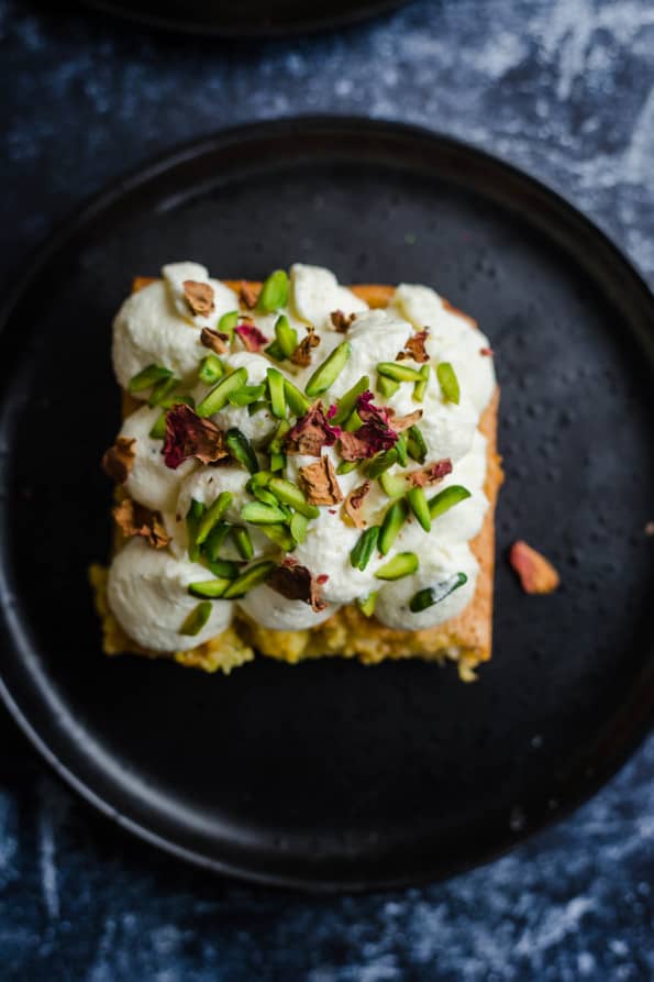 Ras Malai Milk Cake with rose petals and pistachios on black plate