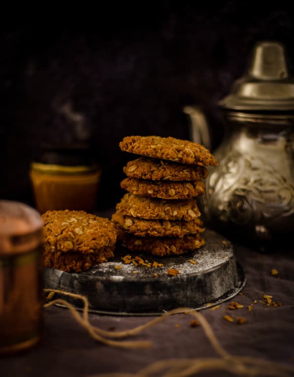 Anzac biscuits in a pile with kettle behind 
