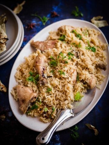 Chicken Pulao in dish with plates and papad to side