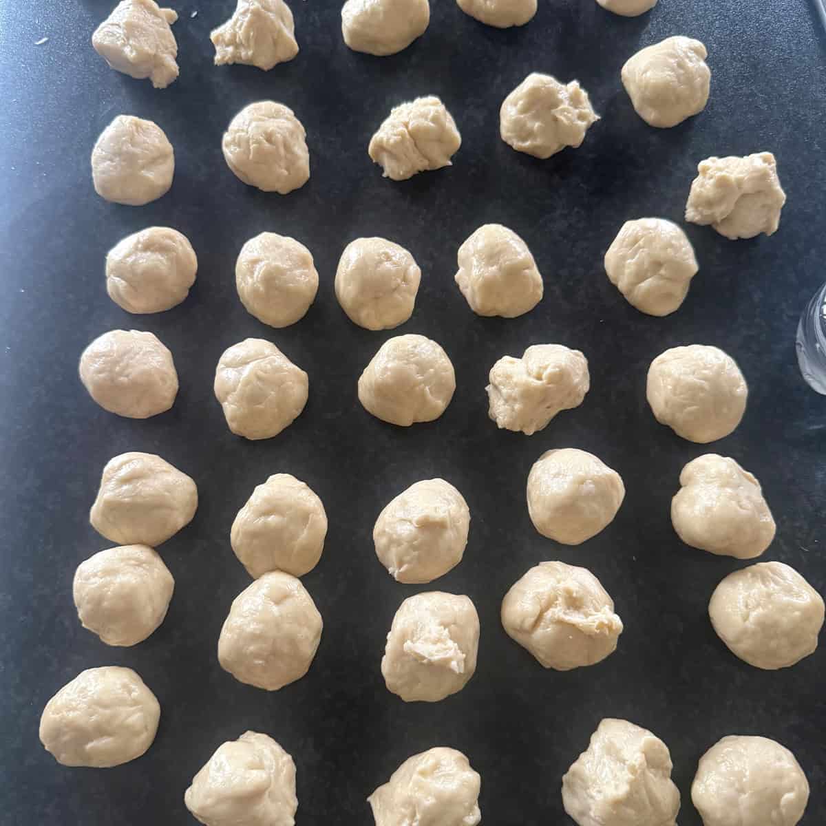 Raw dough balls for Yemeni honeycomb bread on a black surface.