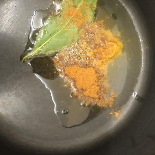 Dry spices added to bay leaf and cumin in pot