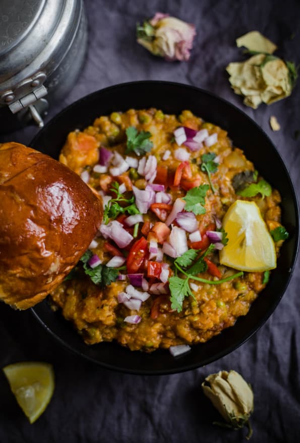 Pav Bhaji in black bowl, with onions and tomatoes, with flowers around it