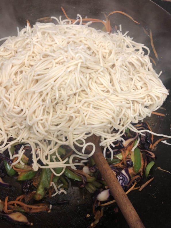 Noodles added to vegetables in wok