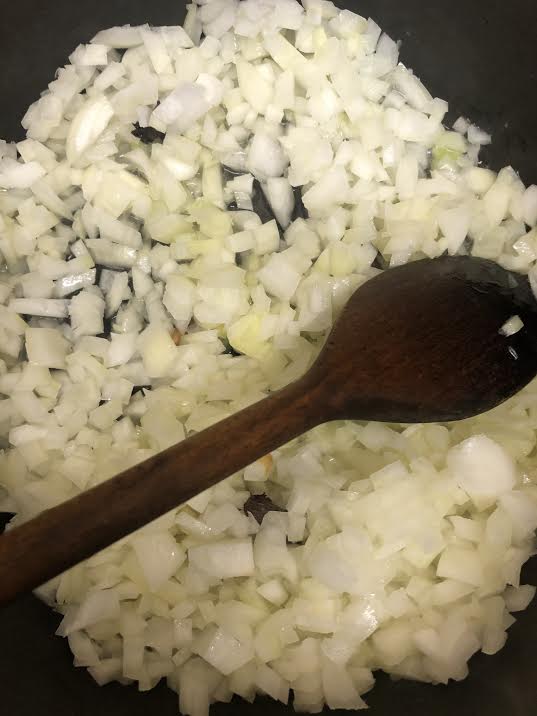 Onions cooking in pot with wooden spoon