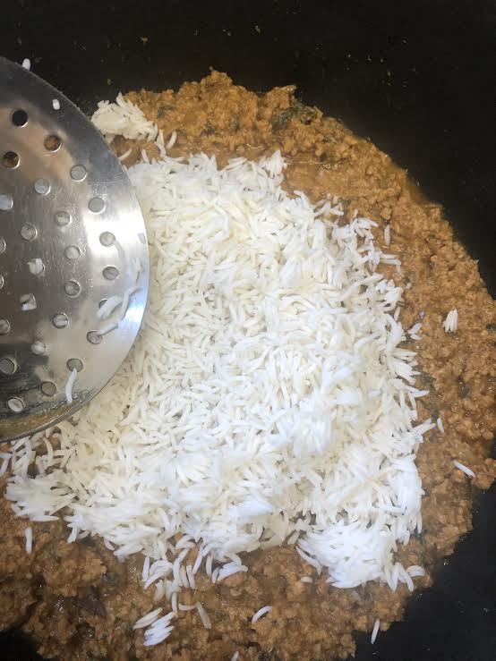 Keema layer with rice being spread over the top with metal spoon