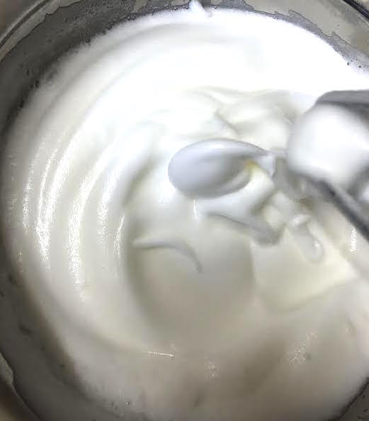 Glossy egg whites in bowl at soft peaks