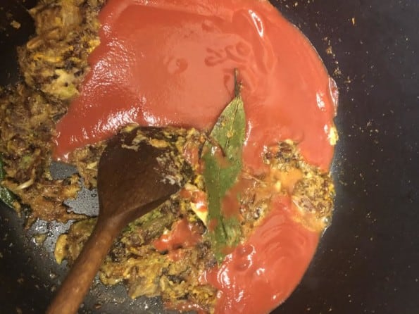 Crushed tomatoes added to pot with wooden spoon