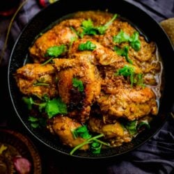 Cooked chicken dish in bowl with coriander on top and spices scattered around the table