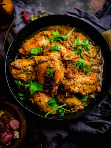 Cooked chicken dish in bowl with coriander on top and spices scattered around the table