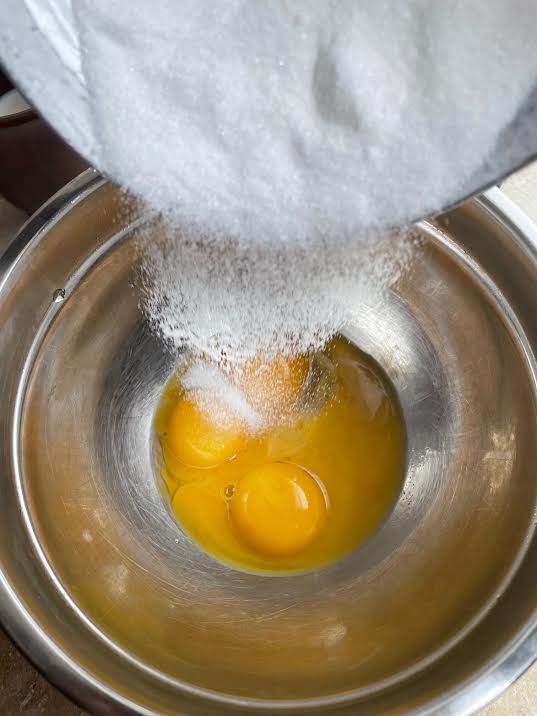Sugar being poured into egg yolks