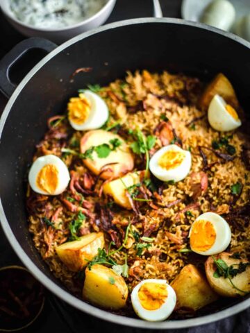 Pakistani Chicken Biryani Recipe in a pot with Eggs on top and salad to back