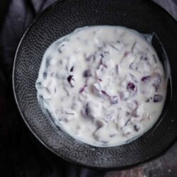 Onion raita in a bowl with a towel to back