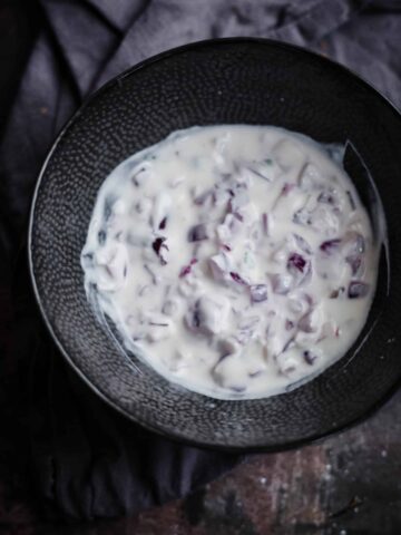 Onion raita in a bowl with a towel to back