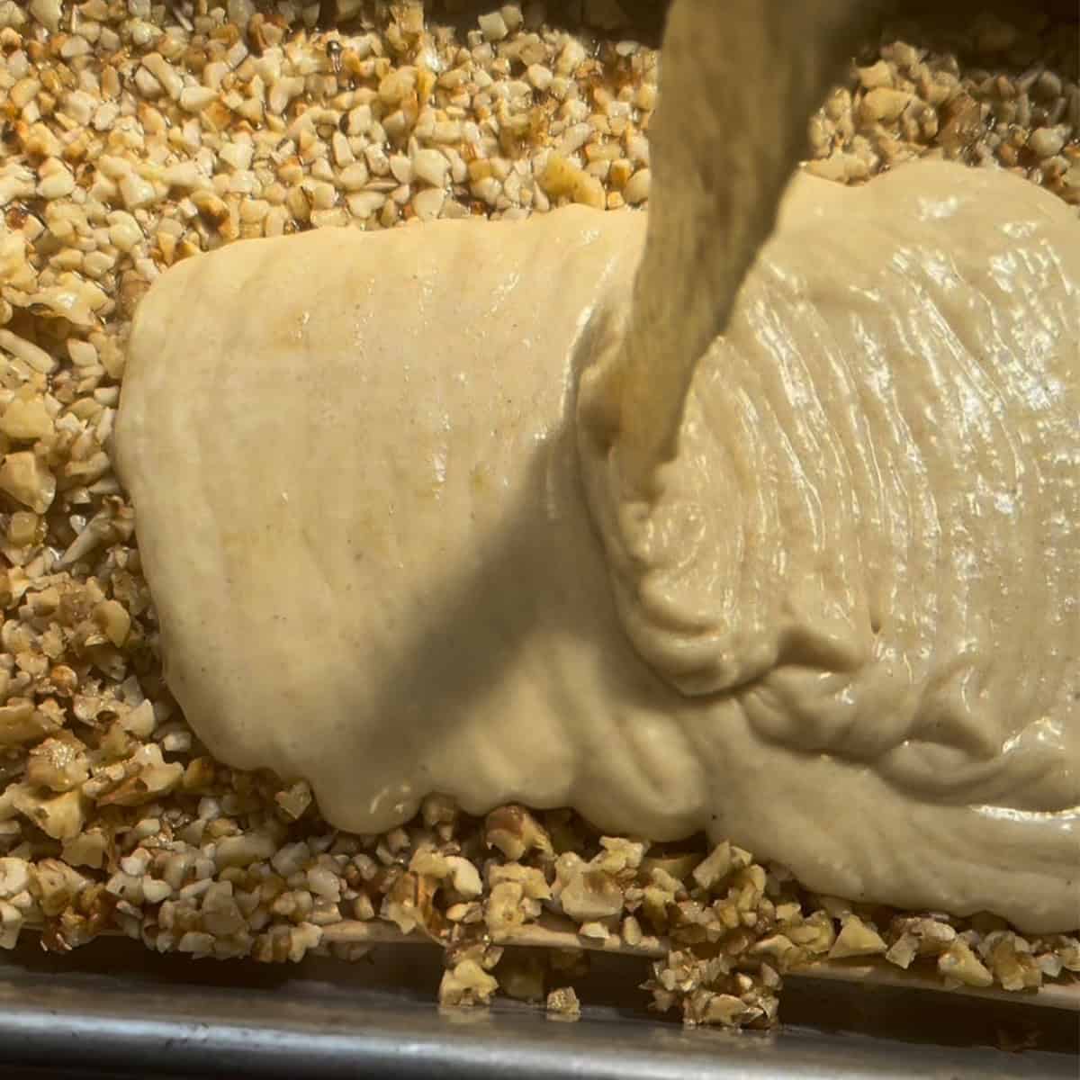 Baklava Cake with Honey Nut Topping & Citrus Cardamom Syrup cake batter being poured onto nut layer
