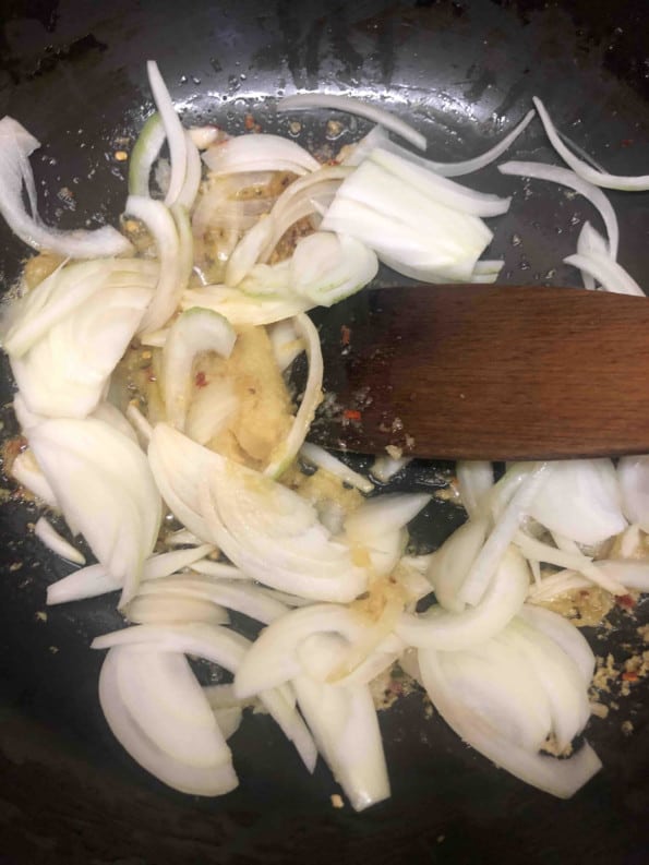 Onions being stirred in wok with wooden spatula